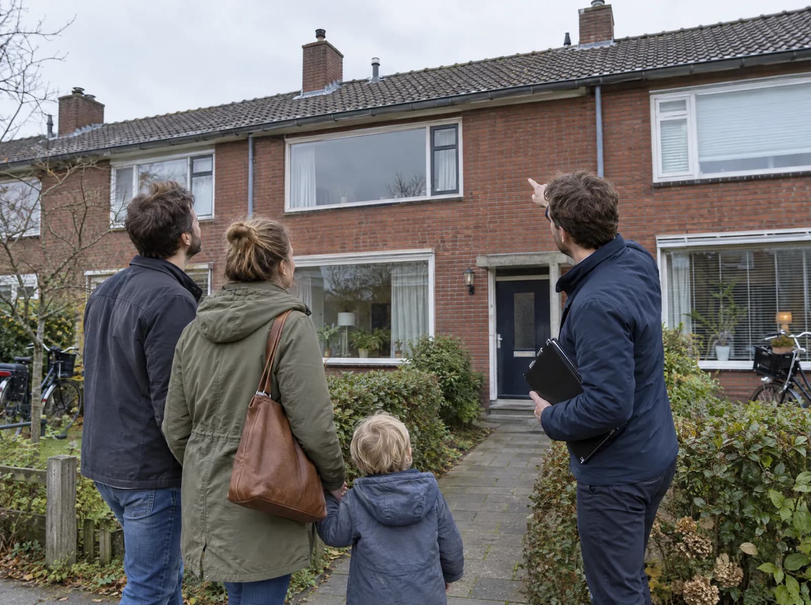 Een jong gezin bekijkt met een makelaar een rijwoning die te koop staat