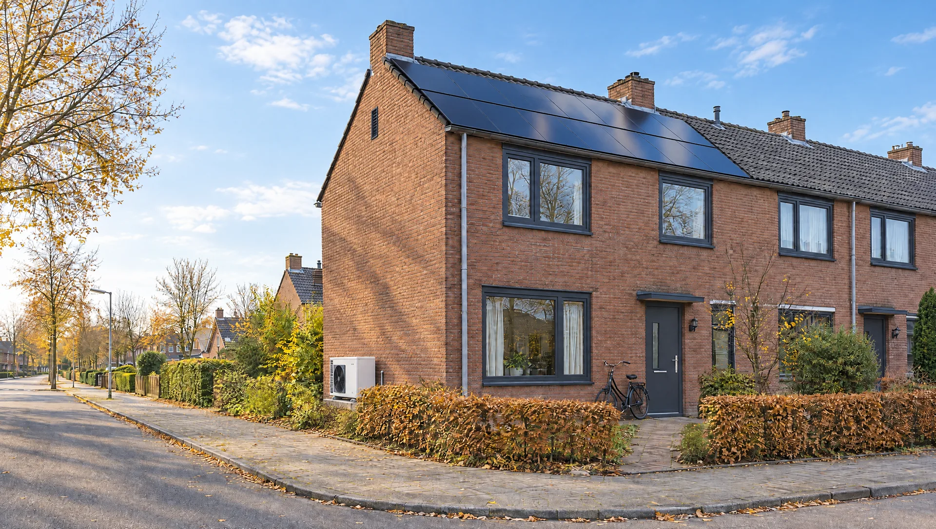 De hoekwoning met zwarte zonnepanelen op het dak, in laag herfstzonlicht